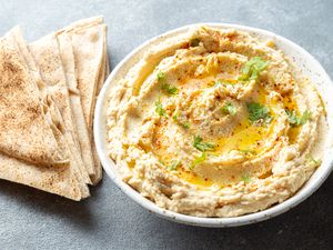A bowl of hummus garnished with herbs and spices accompanied by pita bread