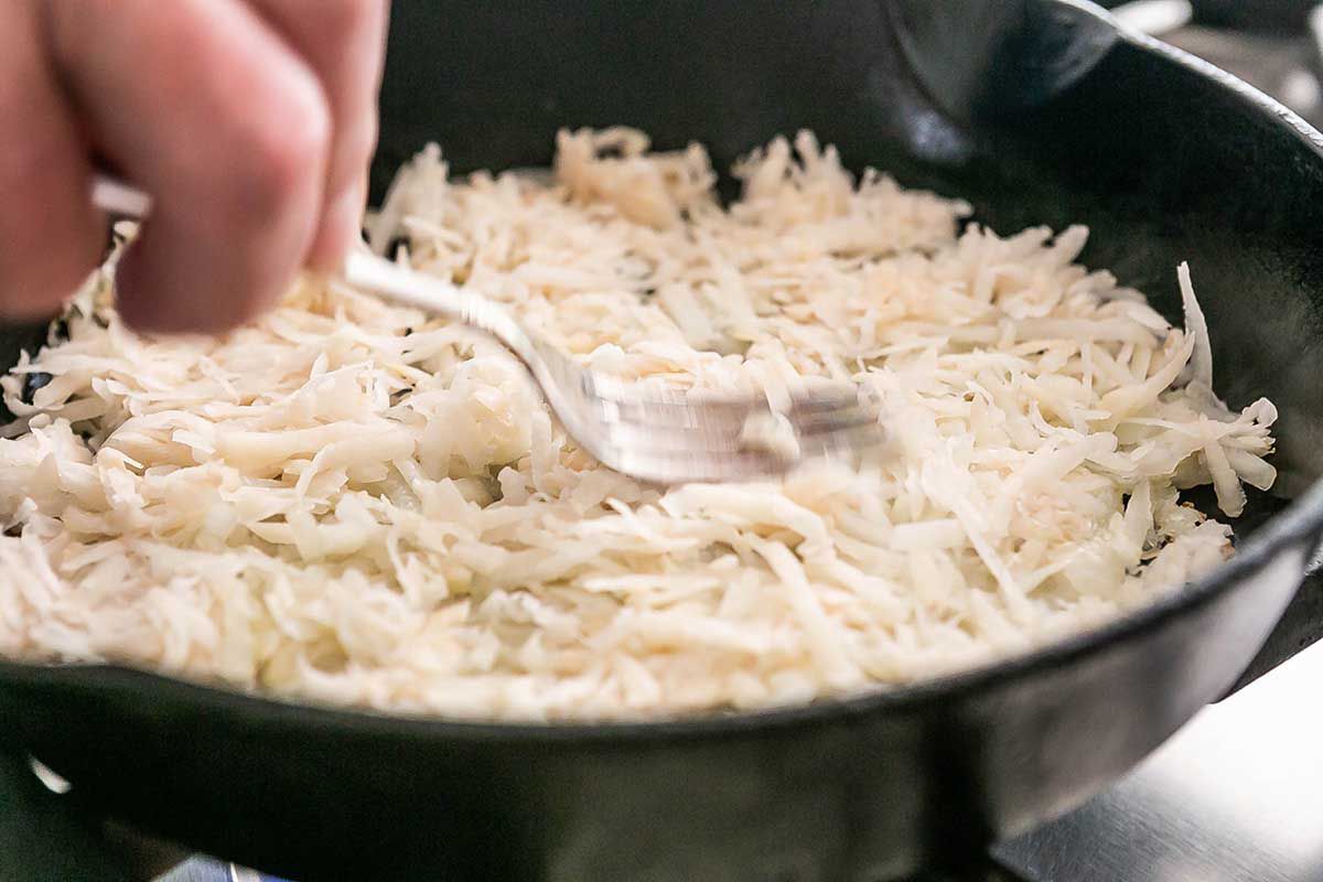Shaved potatoes being stirred with a fork on a cast iron