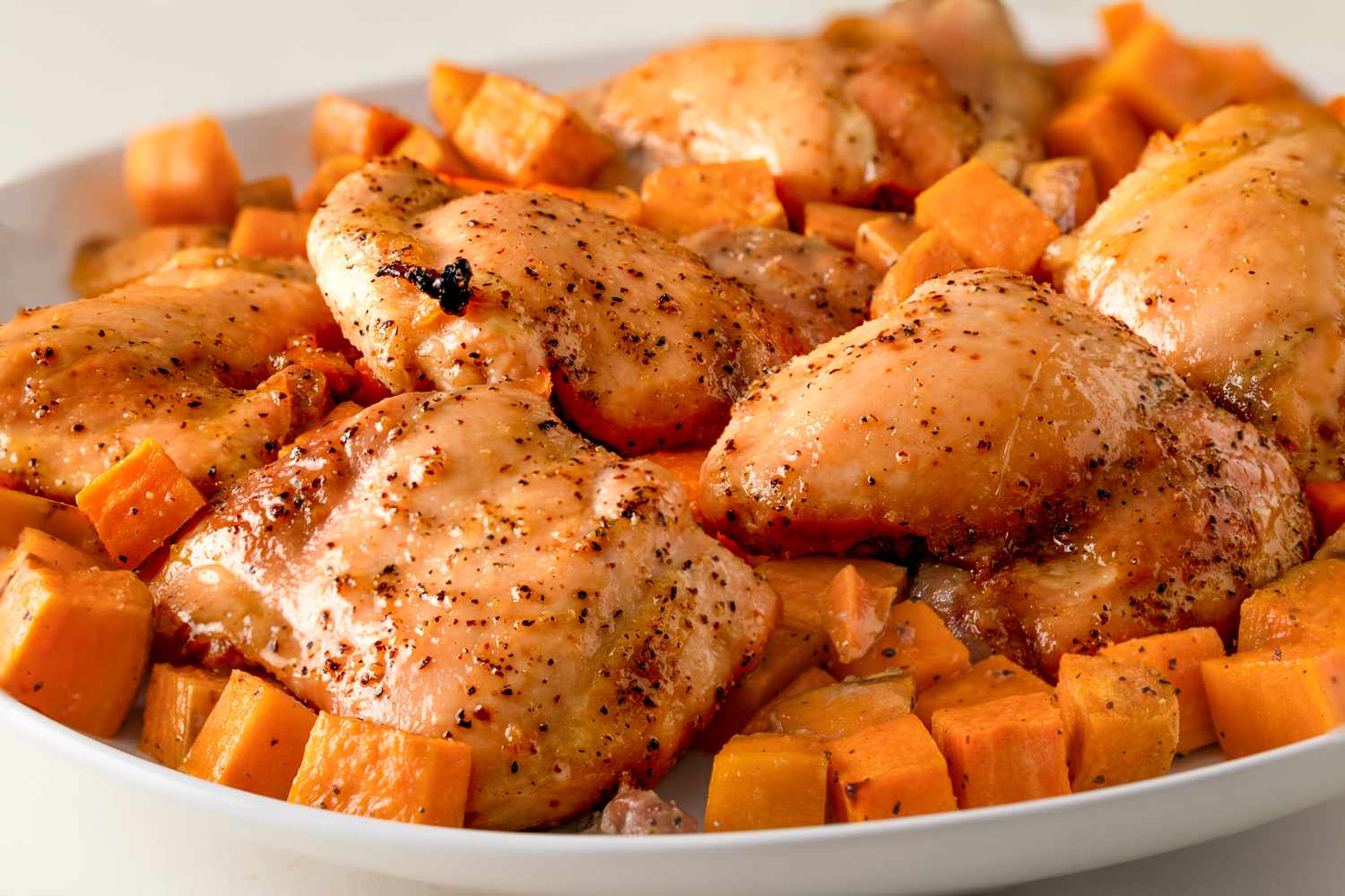 Side view of a white platter of roasted chicken and sweet potatoes recipe