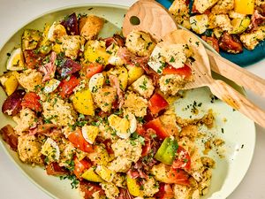 Platter with a salad of bread cubes, tomatoes, zucchini, and herbs, wooden serving utensils on the plate