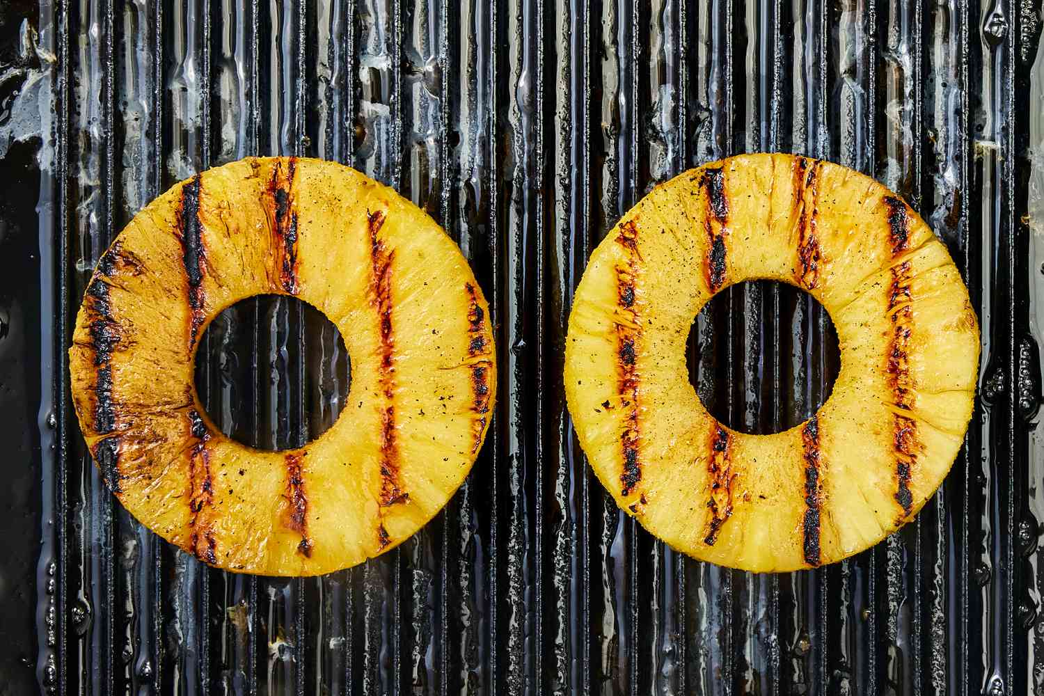 Two pineapple slices on a grill with grill marks for Huli Huli Chicken recipe