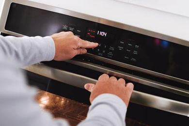 Hands adjusting the controls on an oven to preheat