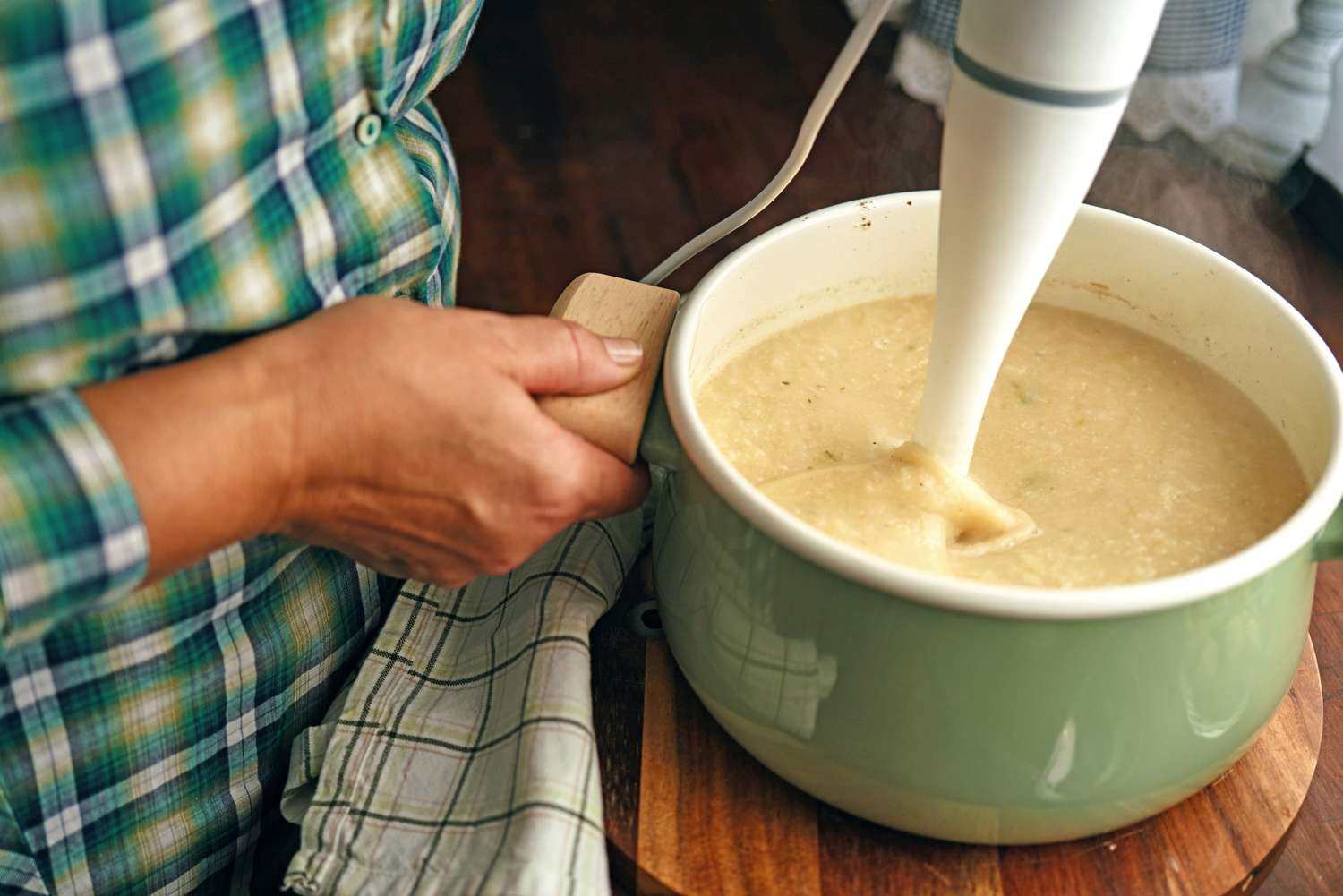 A hand holding a pot handle while blending soup in a pot with an immersion blender
