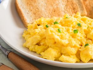 Close up of scrambled eggs topped with chives on a white plate next to pieces of toast