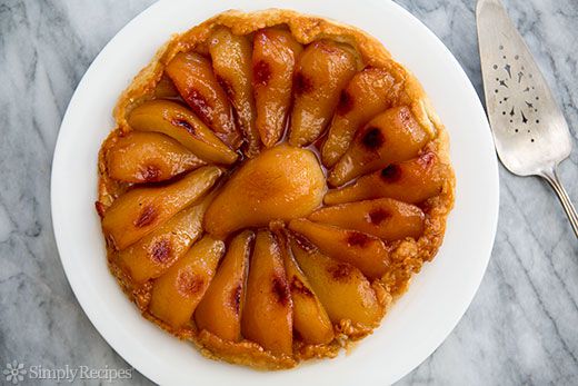 A whole pear tarte tatin on a plate, ready to slice and serve