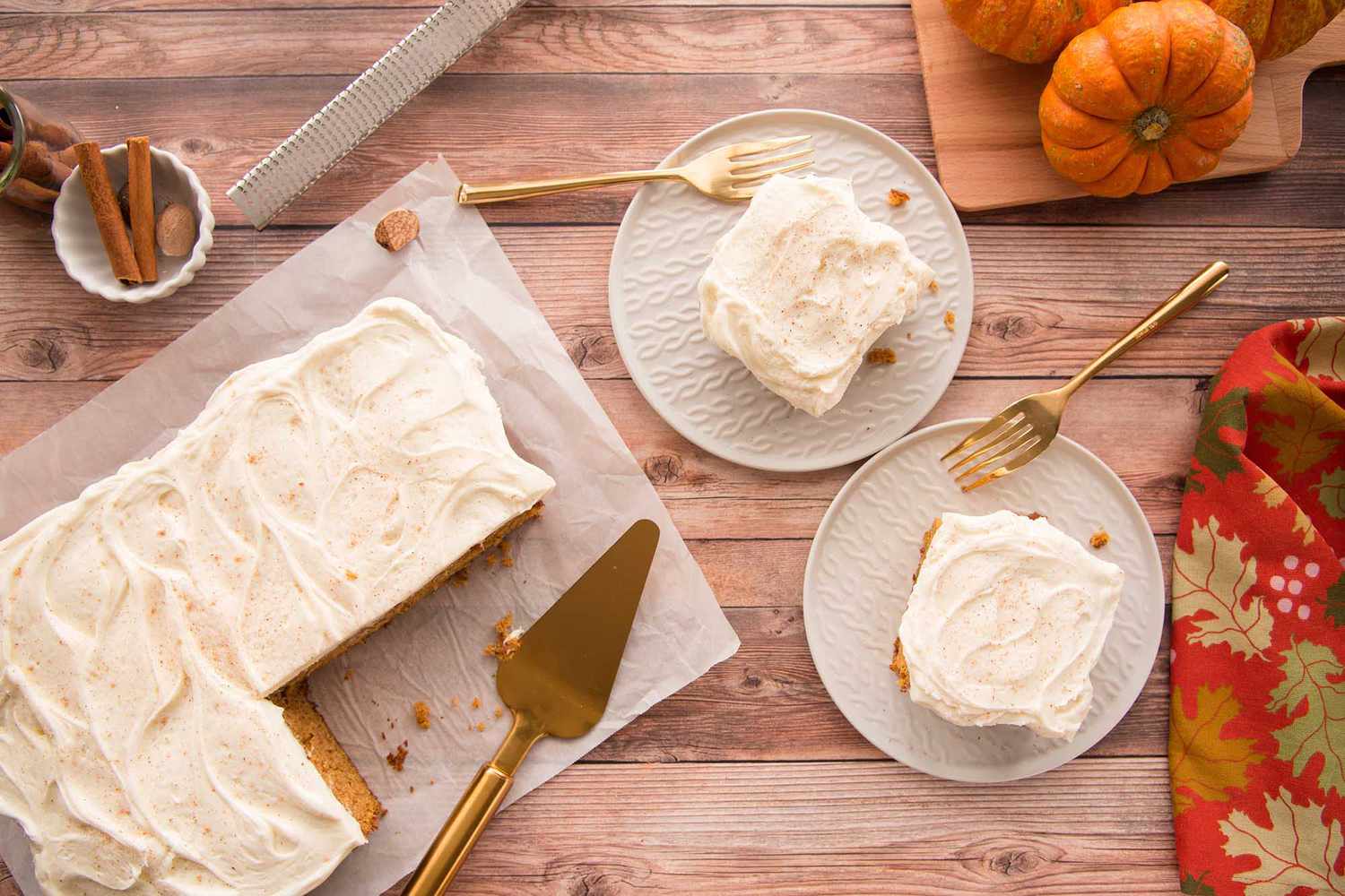 Pieces of pumpkin cake with cream cheese frosting cut from a sheet pan and put on plates