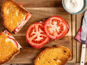 Open tomato sandwich with a side of mayonnaise on a wooden board