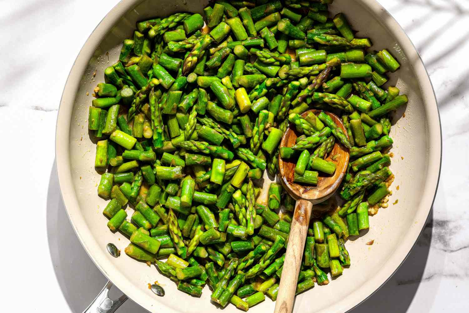 Sautéed asparagus in a skillet with a wooden spoon.