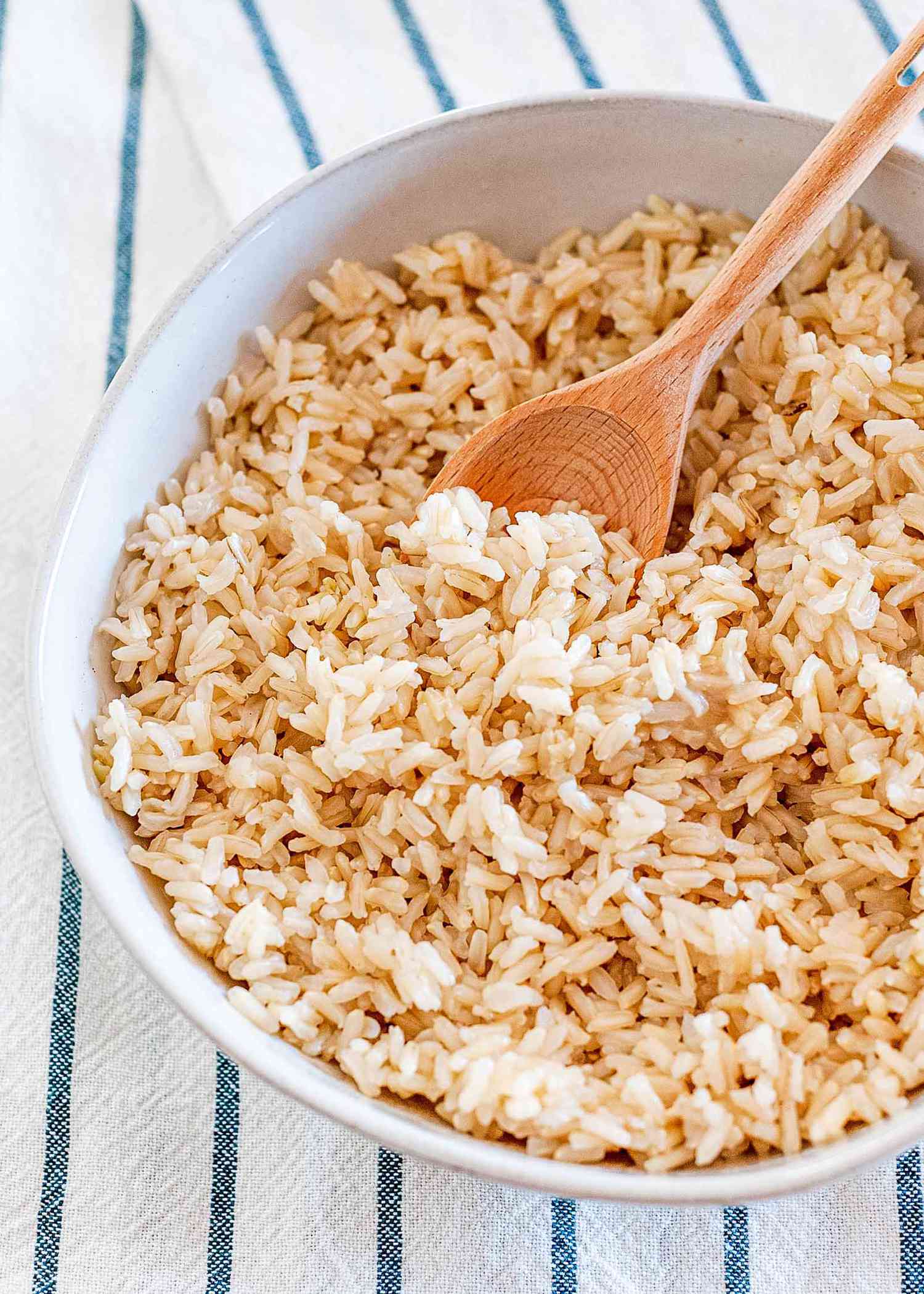 Long grain Brown rice cooked on a stove top in a white bowl with a wooden spoon