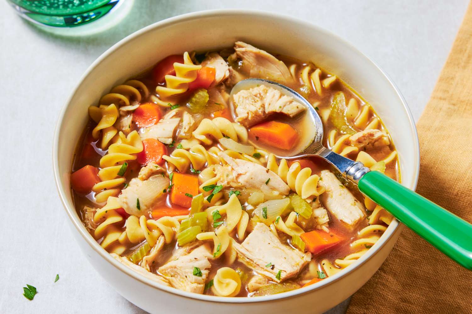 A bowl of turkey noodle soup with spiral pasta chunks of turkey carrots and celery served with a spoon