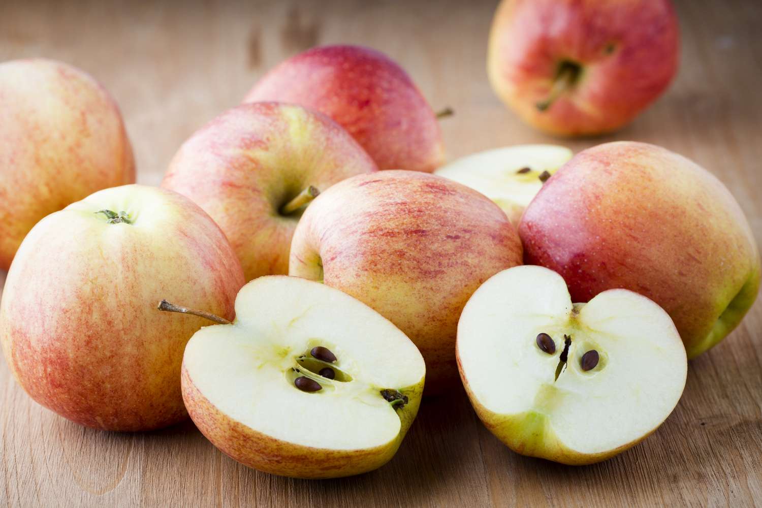 Various whole and halved apples arranged on a wooden surface