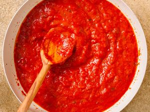 A wooden spoon in a bowl of tomato sauce evenly spread and textured