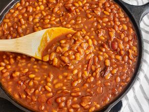 A skillet filled with baked beans being stirred with a wooden spoon