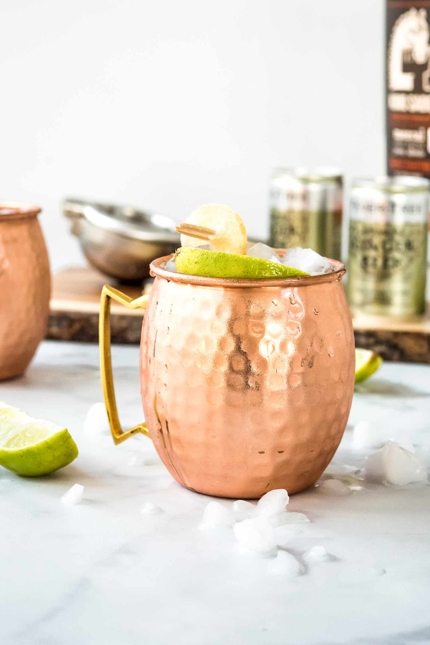 Mezcal Mule in a Copper Mug Surrounded by Ice and Limes. More Ingredients in the Background