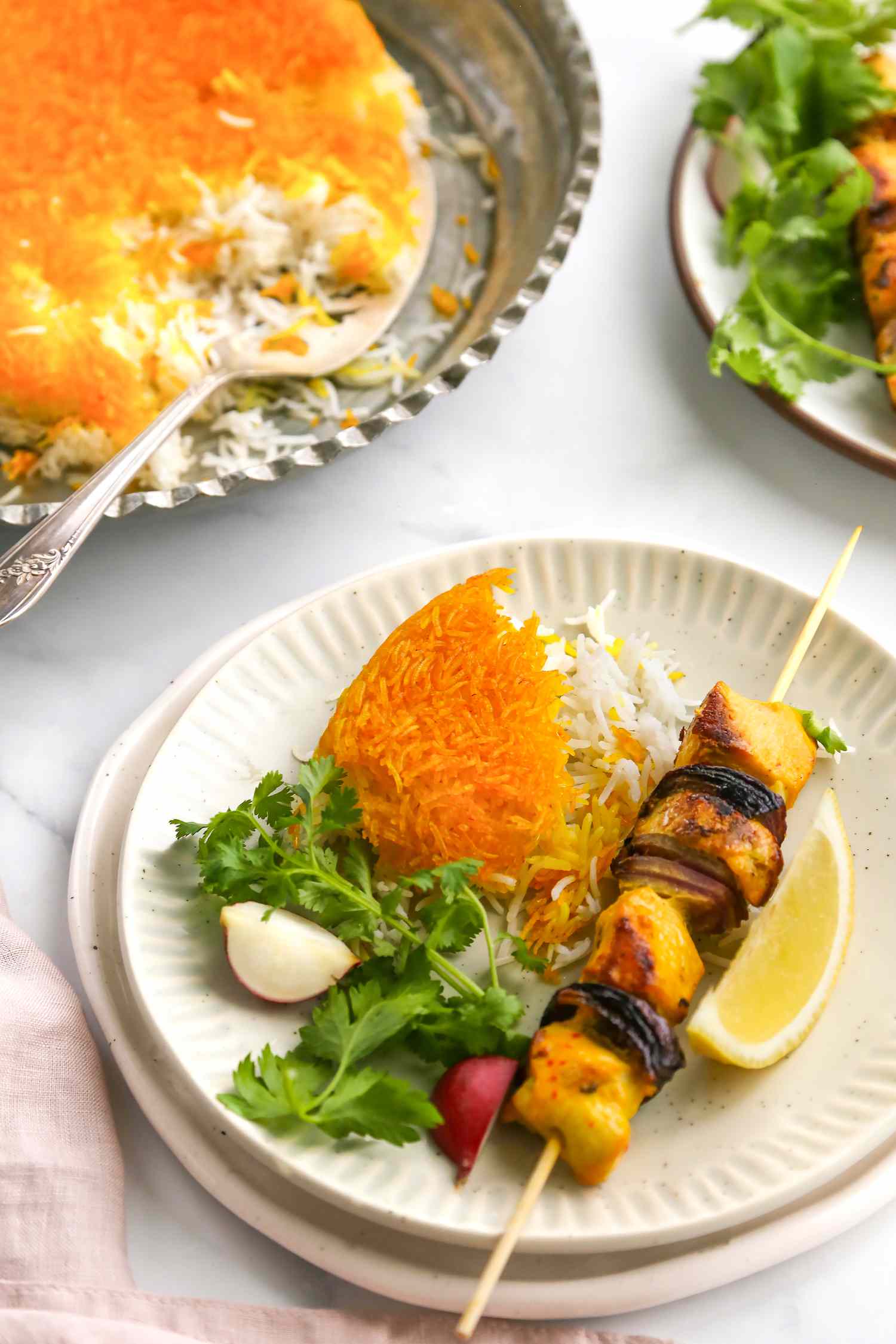 Tahdig Served with a Kebab, a Side Salad, and a Lemon Slice. In the Background, a Platter with More Tahdig and a Plate with Another Serving