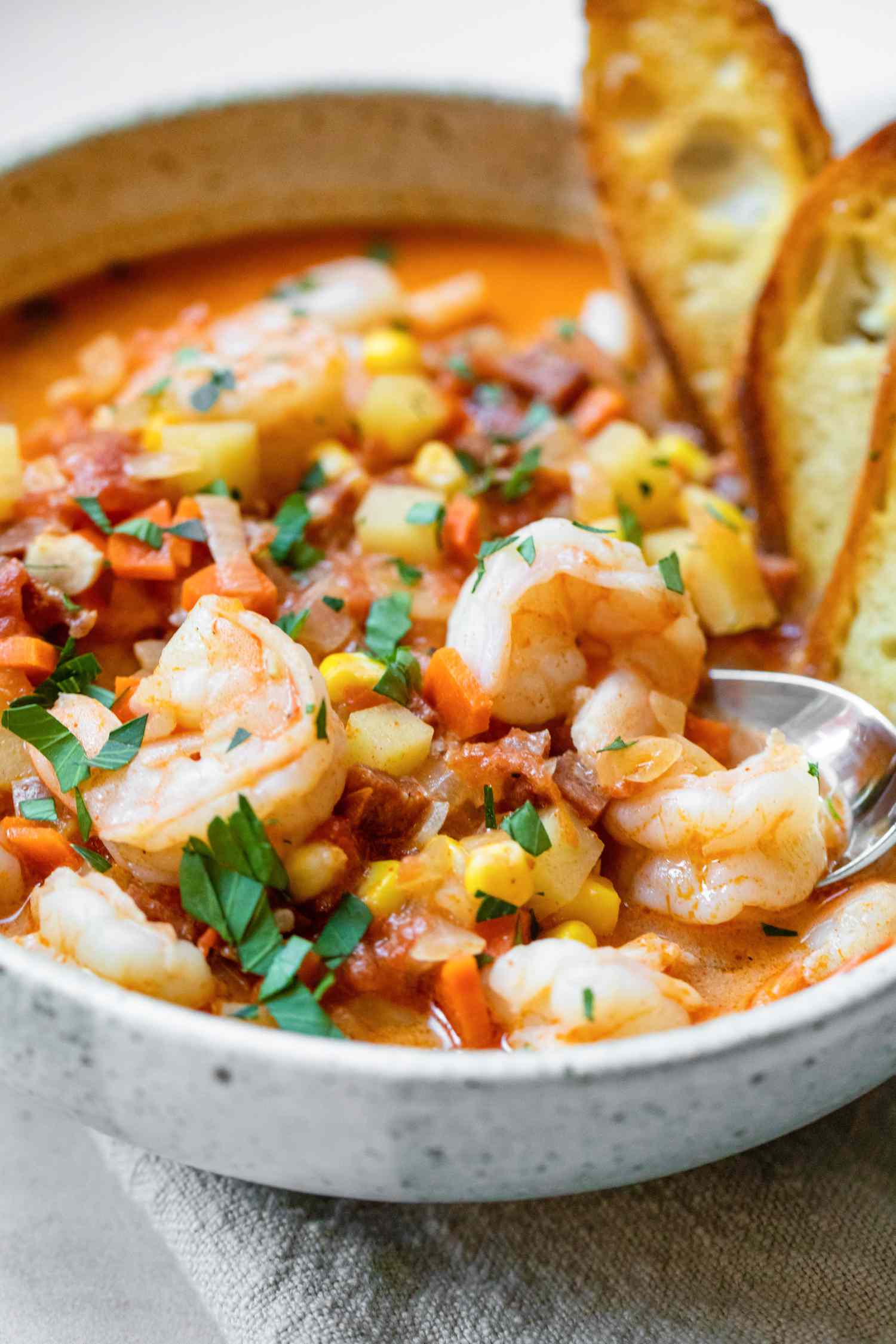 Bowl of Shrimp and Chorizo Chowder Topped with Parsley and Slices of Toasted Baguette, on a Dinner Napkin
