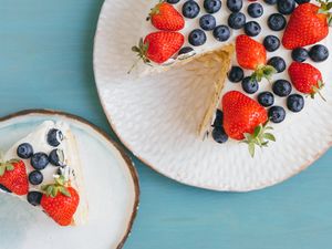 A cake with strawberries and blueberries, slice served separately