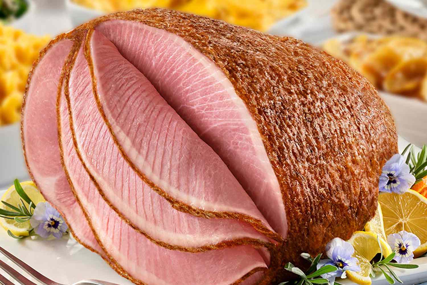 Closeup of a Honey Baked spiral cut ham on a platter with lemon slices and flowers