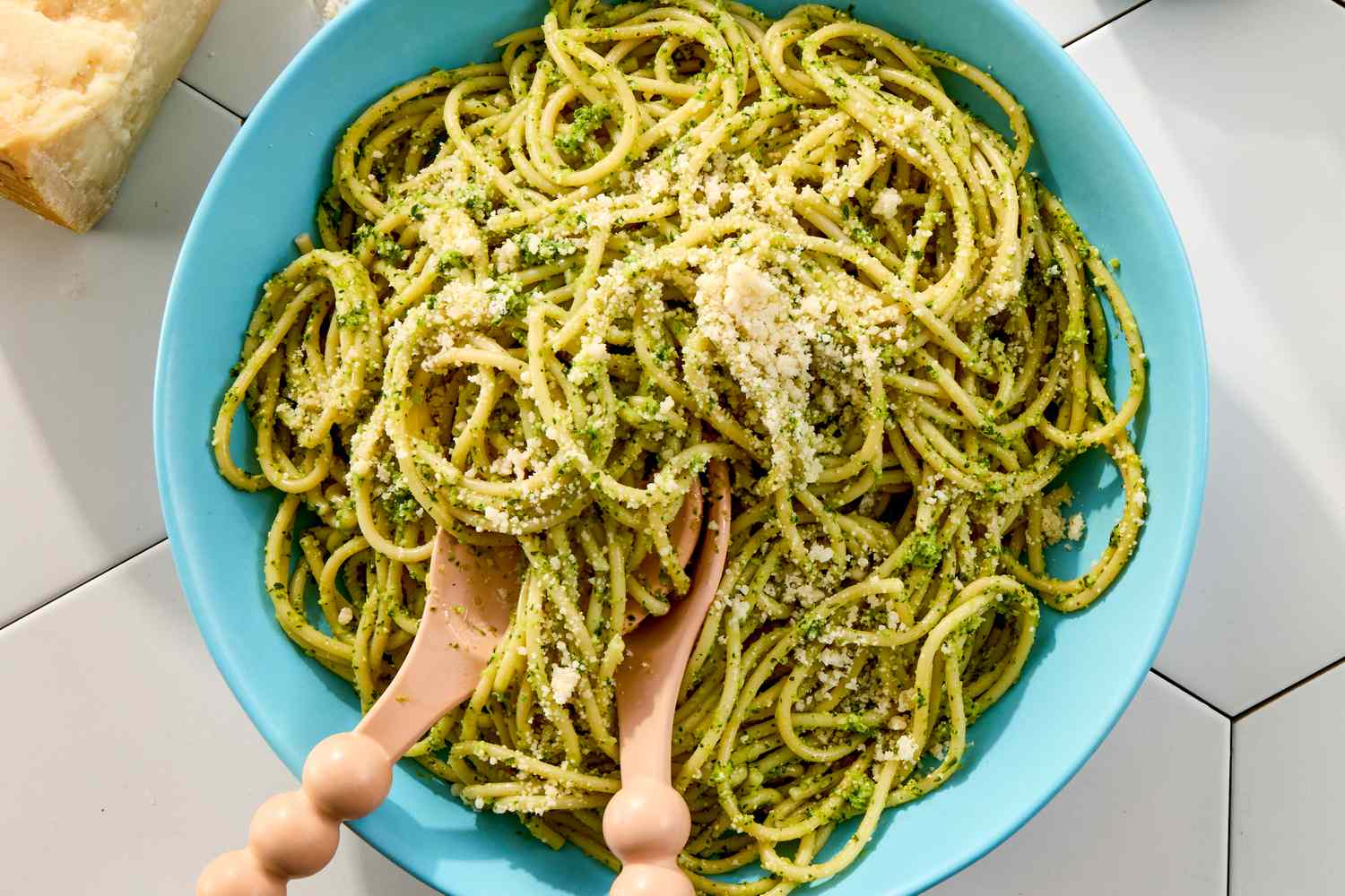 A bowl of pasta coated with broccoli pesto garnished with grated cheese with wooden utensils placed on top