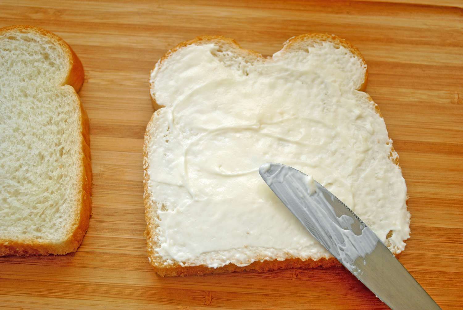 Bread being spread with a creamy substance using a knife preparing for a sandwich
