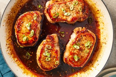 Cooked pork chops garnished with sliced green onions in a pan of sauce