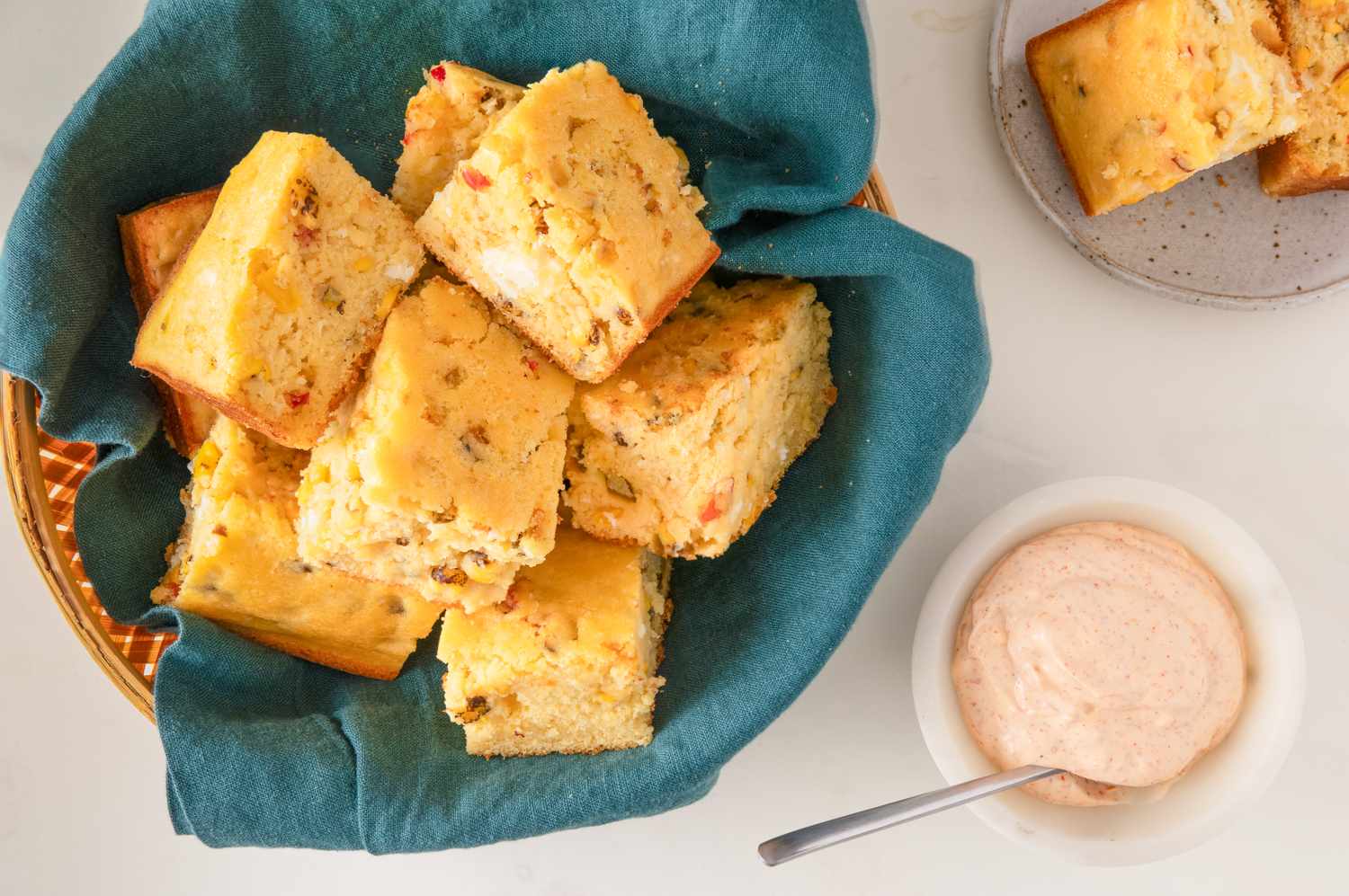 A basket of cornbread pieces with a small bowl of dipping sauce nearby