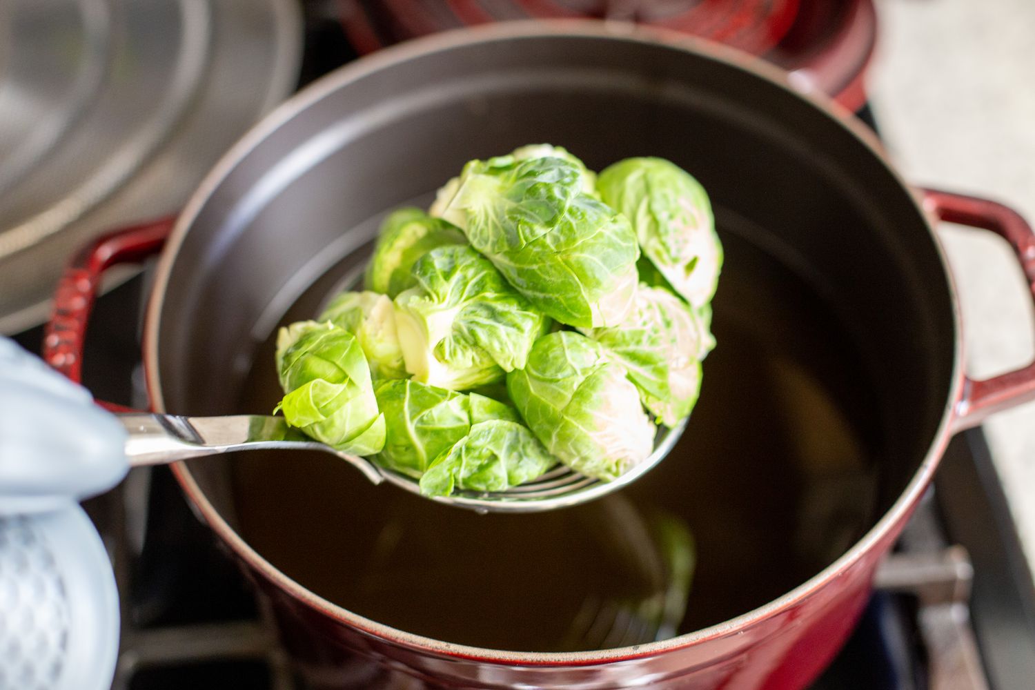 Brussel Sprouts on a Spider Strainer Carefully Placed in Pot of Hot Oil for Deep Fried Brussel Sprouts Recipe