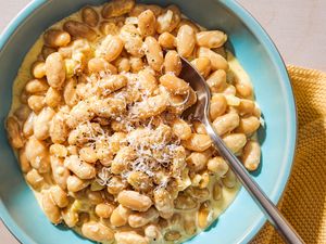 Overhead view of a teal colored bowl of Alfredo Beans with a spoon and topped with shredded Parmesan