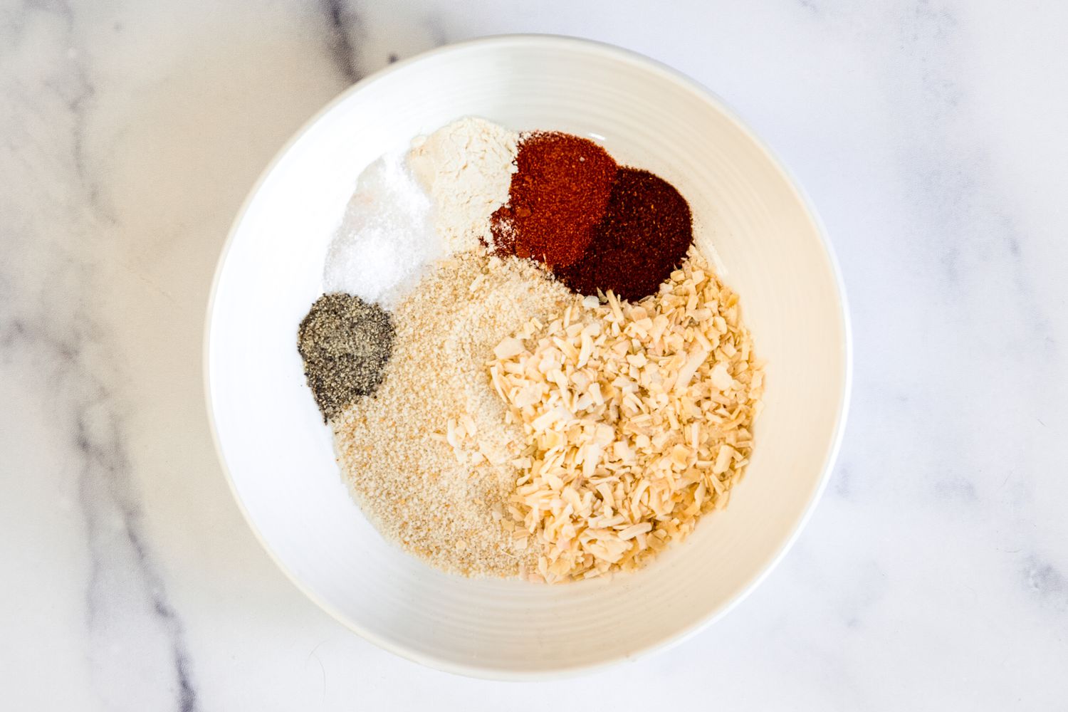 Spices and breadcrumbs in a bowl to make mini meatloaves with veg and potatoes in a sheet pan.