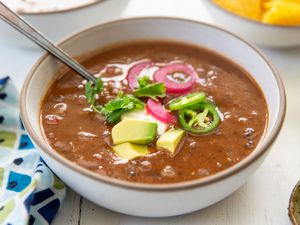 A bowl of 15-minute black bean soup, topped with avocado cubes, jalapeño slices, pickled onion and and cilantro