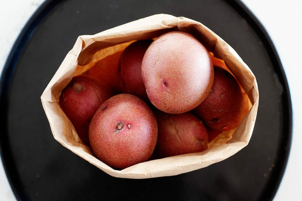 A brown paper bag with yellow potatoes on a black tray.