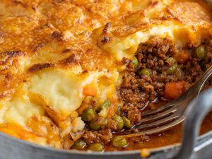 Shepherds pie with a fork in a serving in a pan showcasing layers of mashed potatoes beef peas and carrots