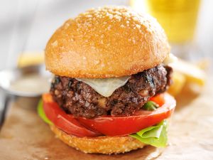 A thick hamburger with lettuce, tomato, and cheese in a bun, placed on a wooden surface with a blurred background