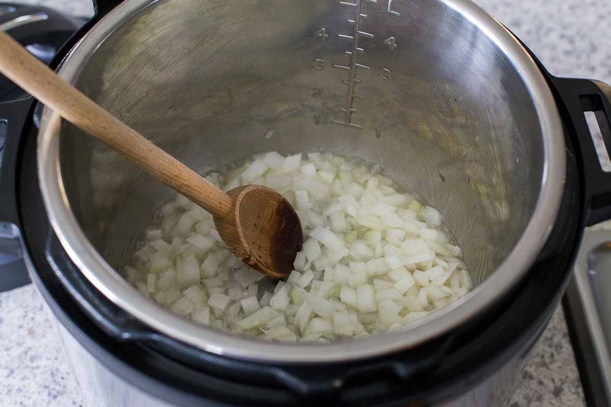Sauteeing onions with a wooden spoon in the insert of an instant pot.