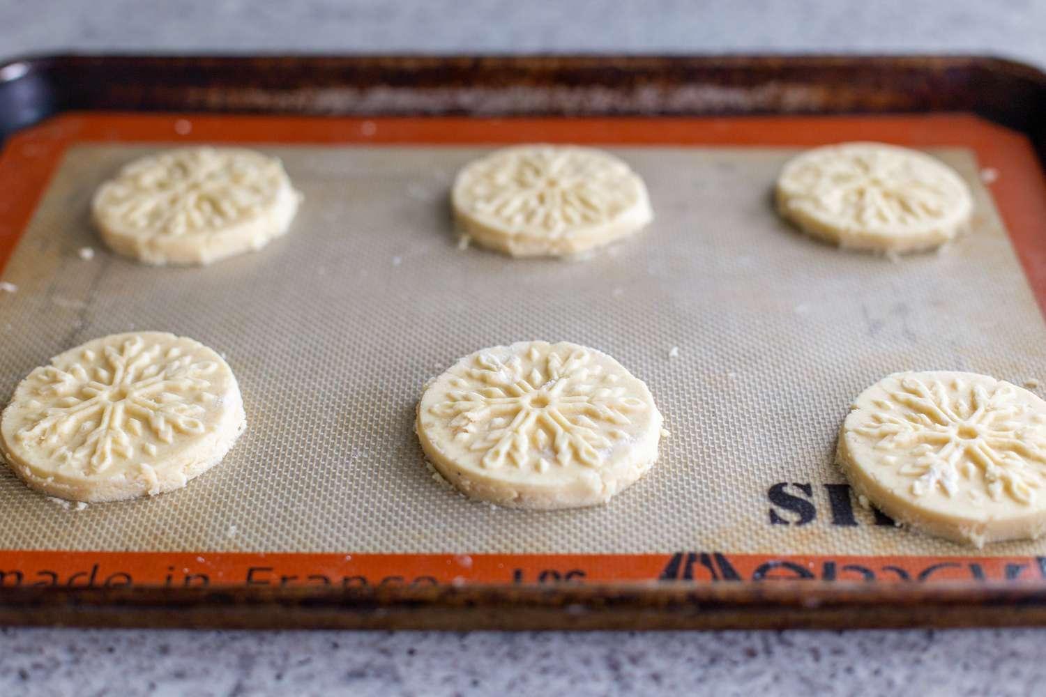 Almond-flavored butter cookies stamped and on a baking sheet.