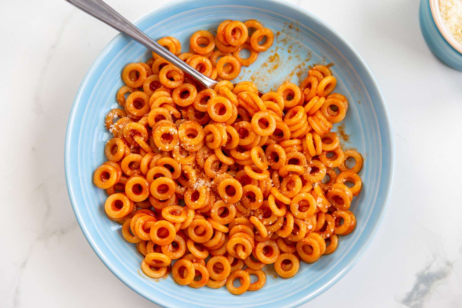 A bowl of spaghetti rings in a tomatobased sauce with a spoon placed on a table