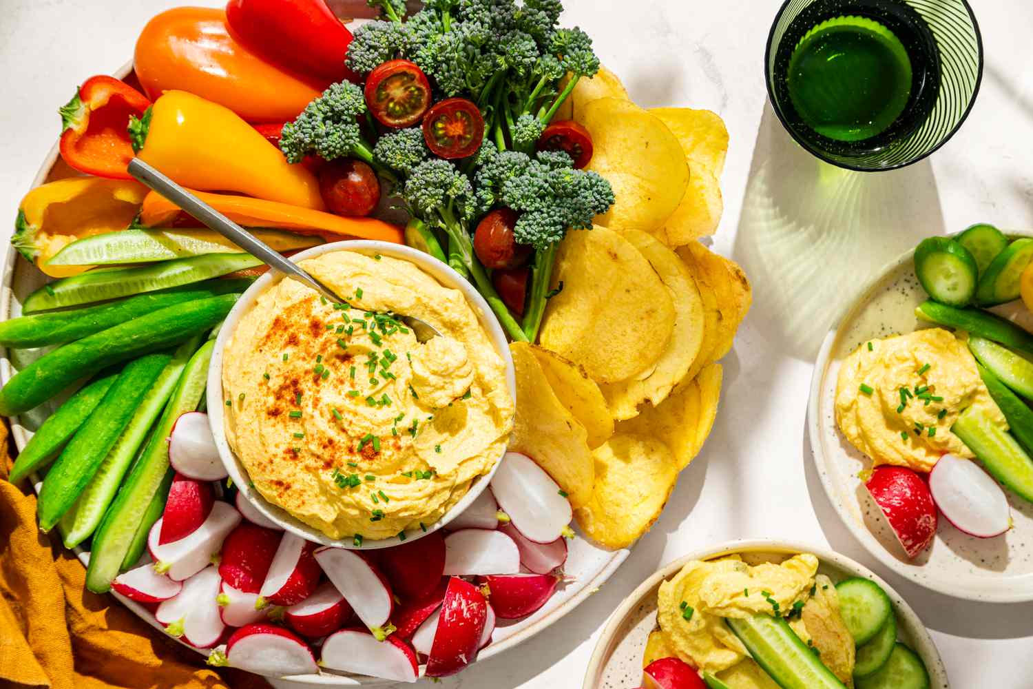 Overhead view of a platter with vegetables and potato chips arranged around a bowl of deviled egg dip and two plates with dip and veggetables