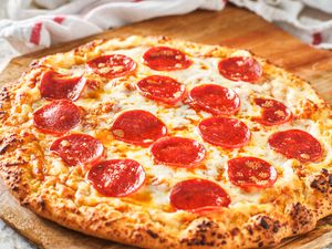 pepperoni pizza on a wooden board surrounded by kitchen towels