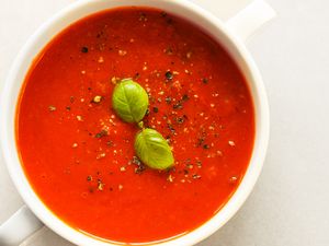 Bowl of tomato soup garnished with basil leaves and black pepper