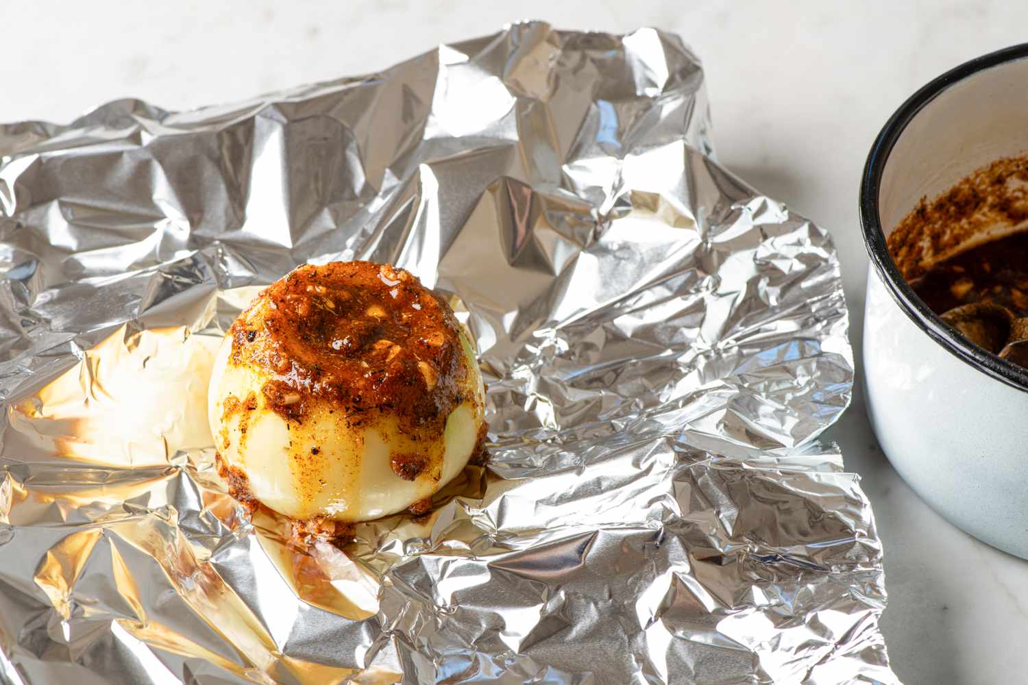 Halved onion with seasoning on foil next to a bowl of marinade or sauce