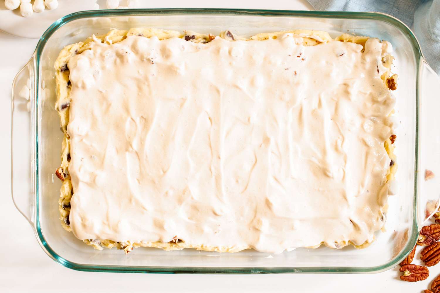 Cookie dough topped with evenly spread out meringue mixture in a rectangular glass baking dish for mud hen bars recipe