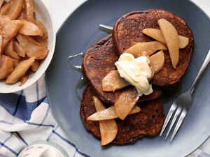 Christmas morning pancakes spread on a plate and topped with pears and creme fraiche. Additional pears are in a bowl next to the plate.