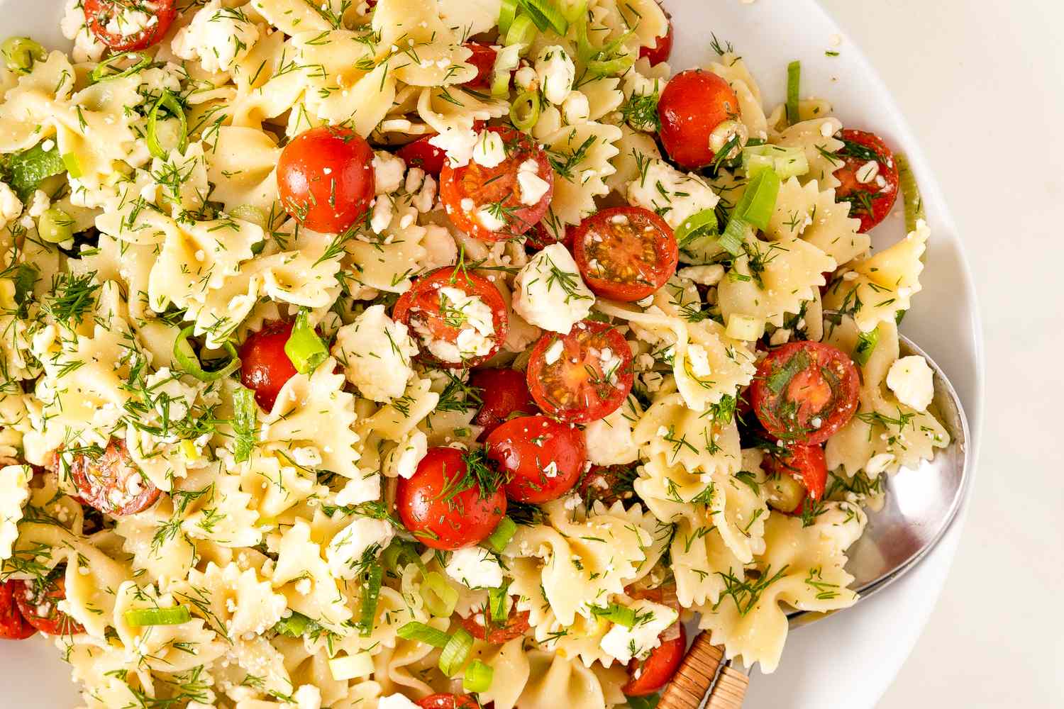 Greek pasta salad with bowtie pasta, tomatoes, and herbs in a bowl