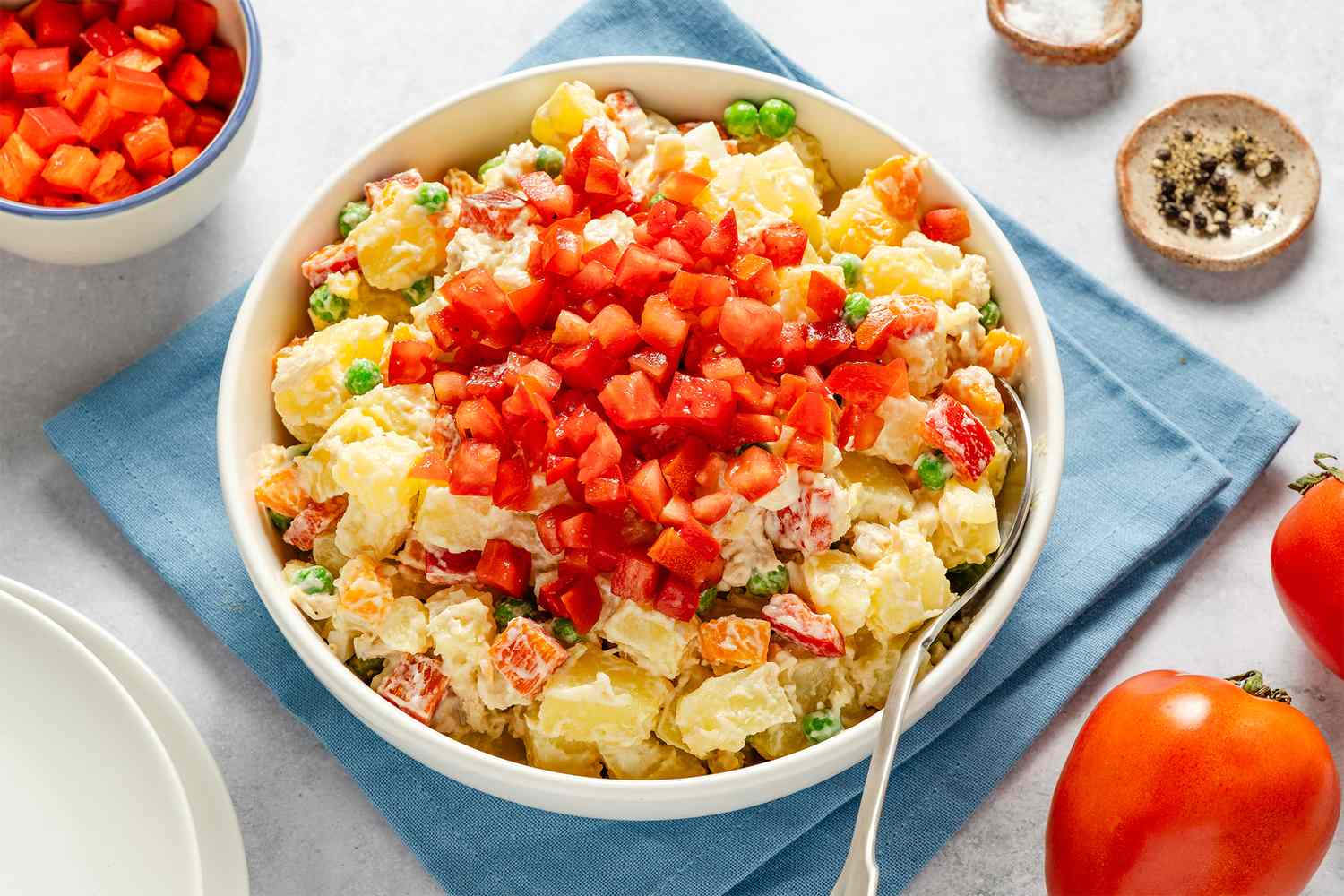 Bowl of salad with diced vegetables on top placed on a blue napkin with tomatoes and seasonings beside it