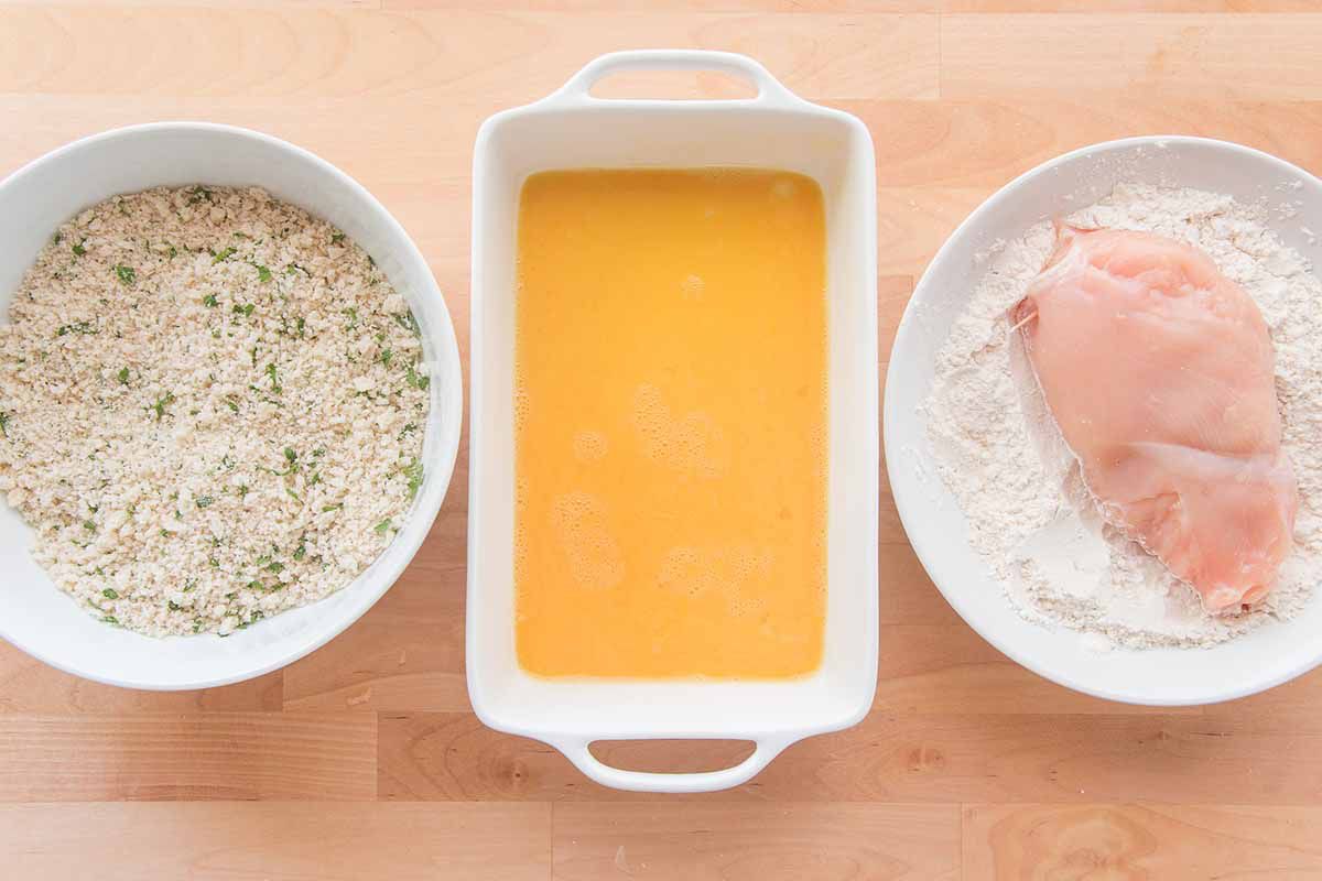 Three dishes lined up to batter chicken cordon bleu -- one with breadcrumbs, one with eggs and another with flour.