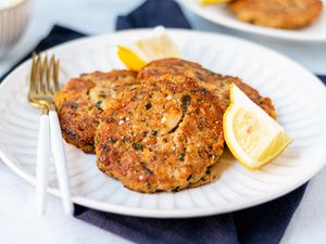 Tuna cakes on a white plate along with a lemon wedge and fork.