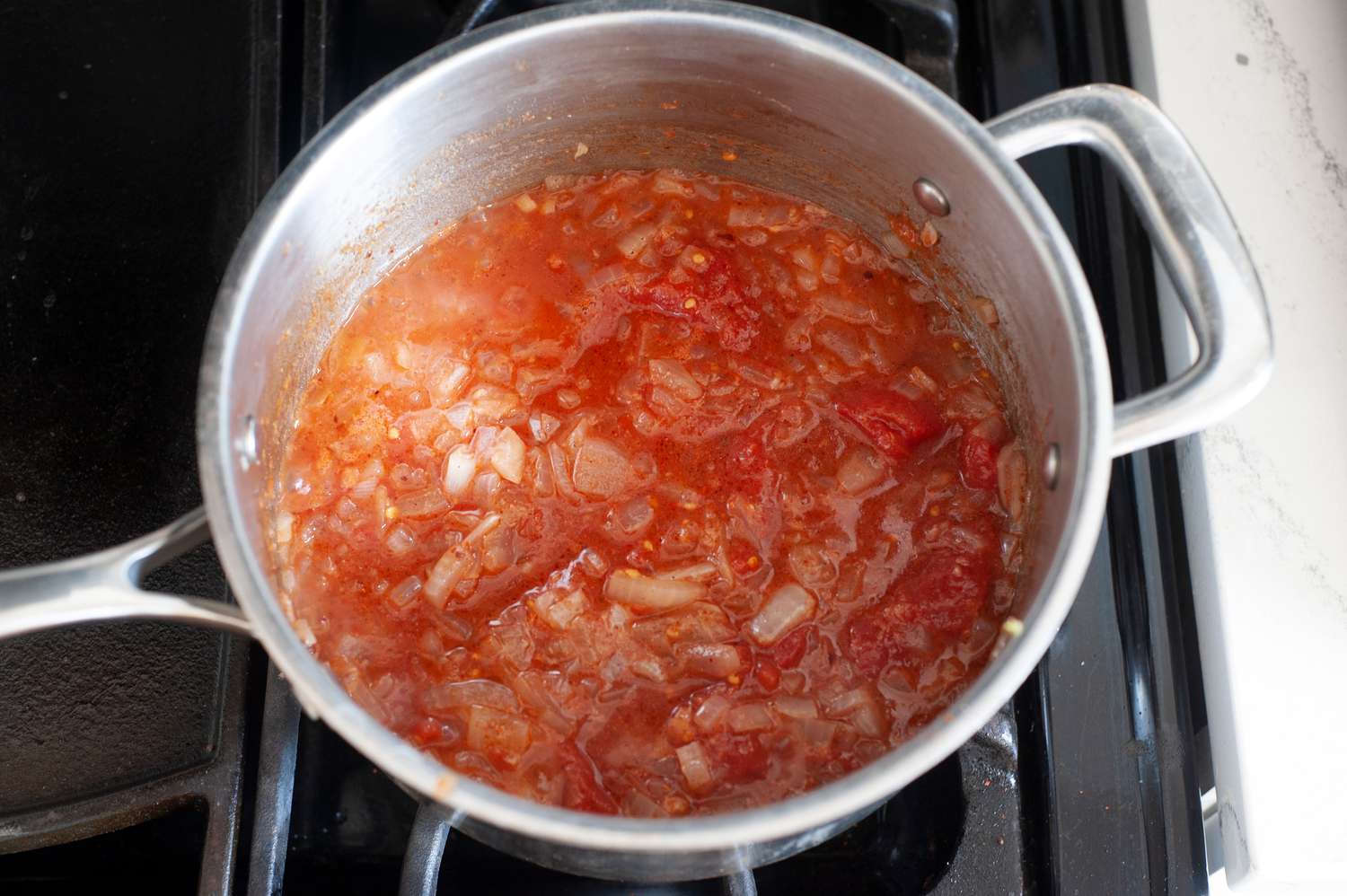 A simmering pot onions and tomatoes to make braised green beans.