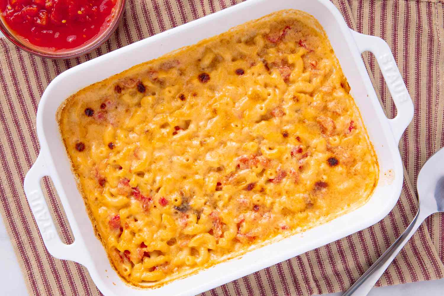 Baked macaroni and cheese in a rectangular dish served with a bowl of tomatobased sauce on the side