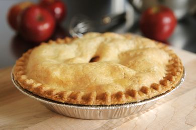 A storebought apple pie on a wooden surface with apples in the background
