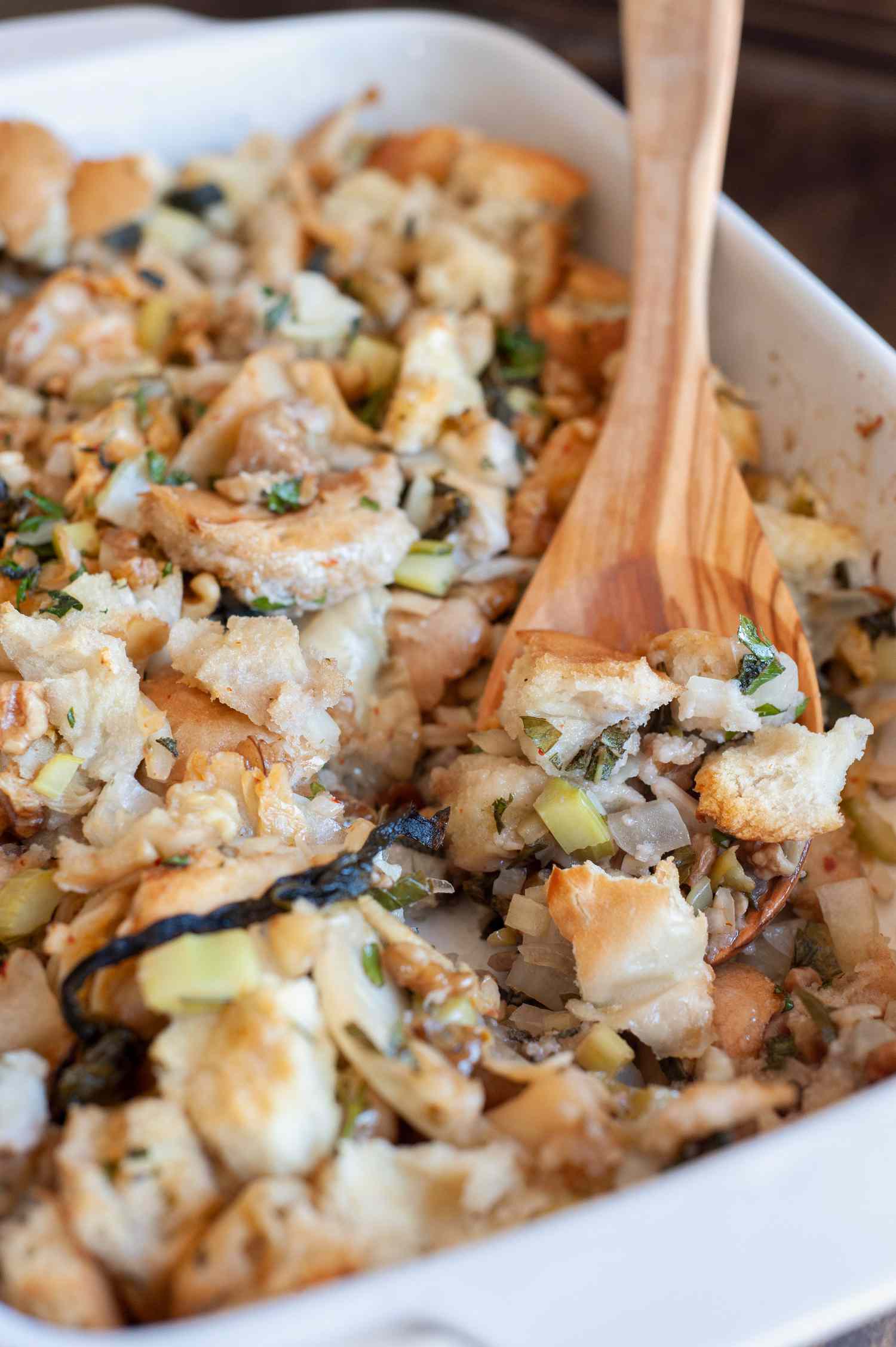 A wooden spoon scooping stuffing out of a dish.